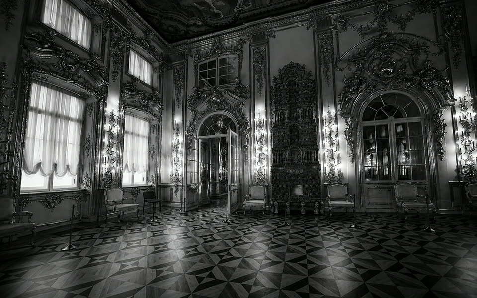 Black-and-white photograph of the Great Hall at the Catherine Palace at Tsarskoye Selo, with gilt-wood panelling, casement windows and star-pattern parquet.