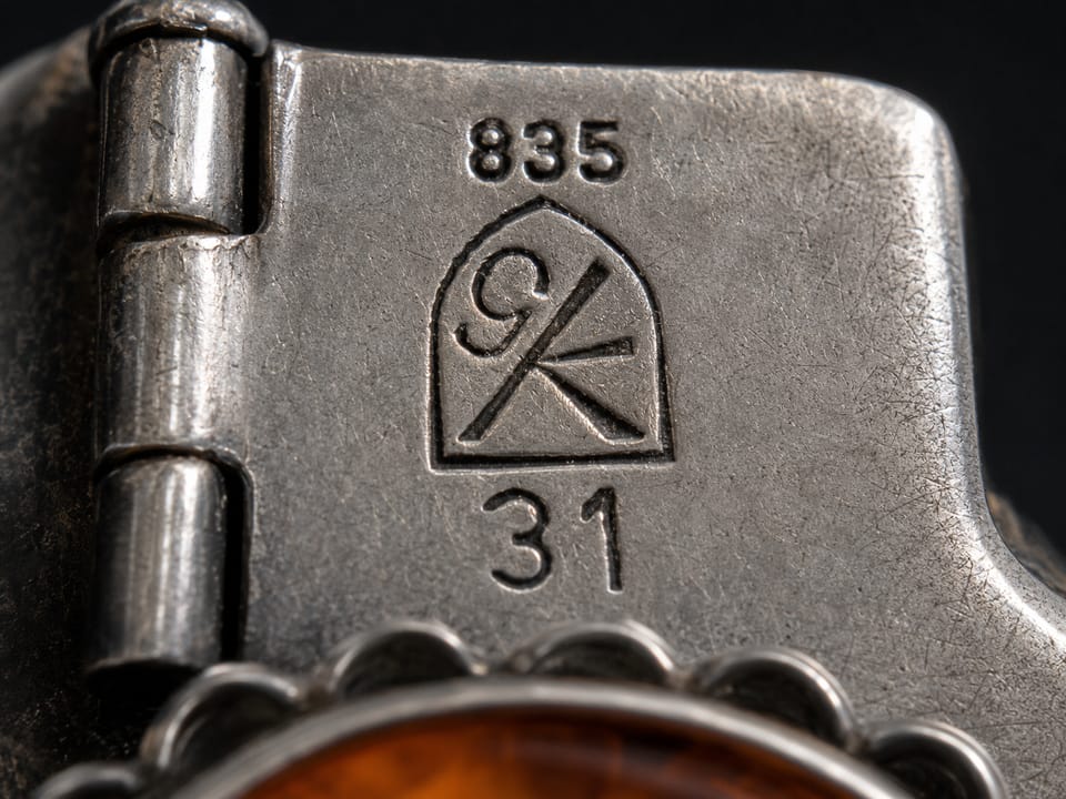 Macro shot of the back of an 835 silver brooch with triple punching: fineness 835, the GK maker's mark in a Gothic-window frame, below it the model number 31