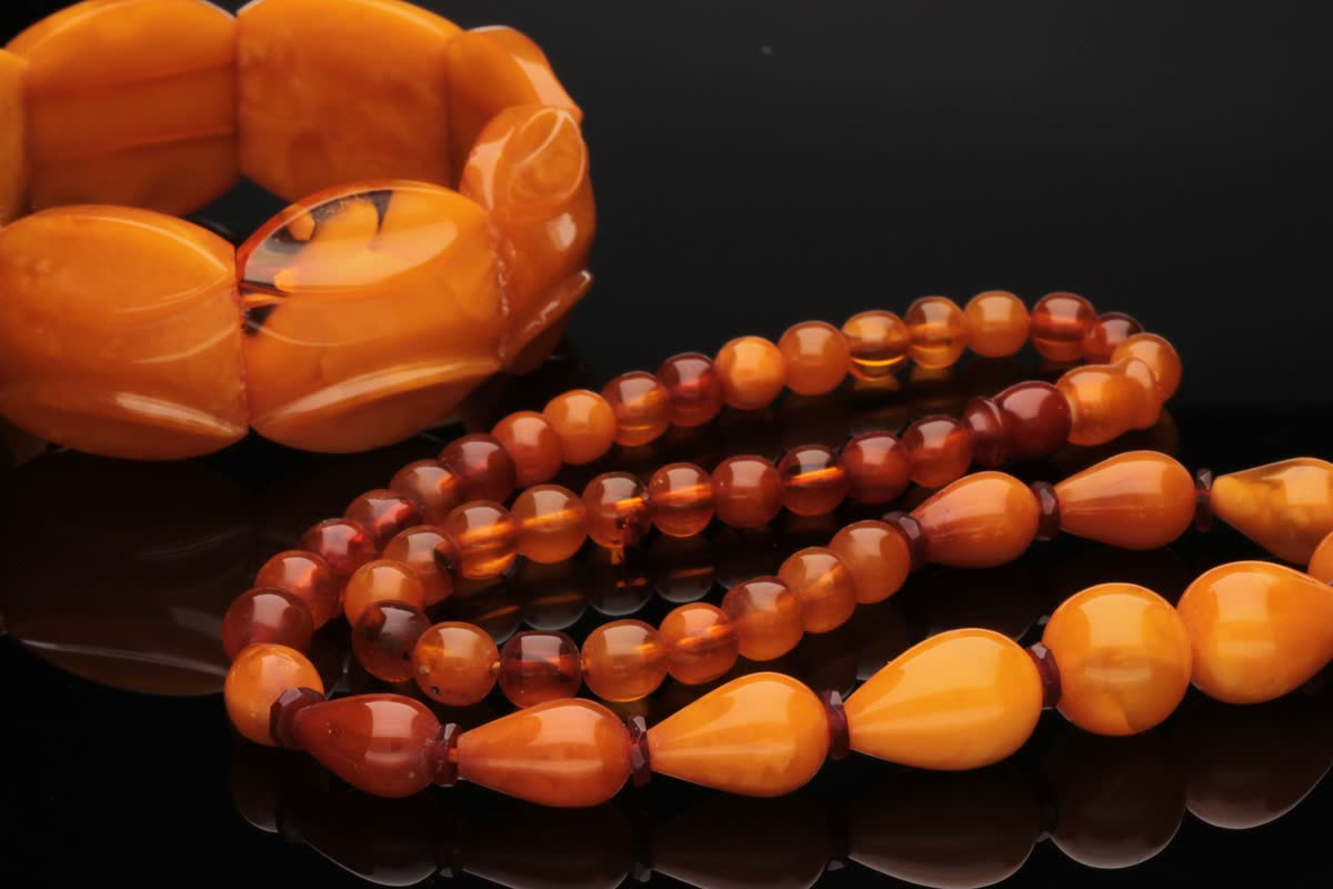 Antikes Bernstein-Gliederarmband mit Butterscotch-Cabochons neben einer Tropfen- und Perlenkette in Naturhonig-Tönen
