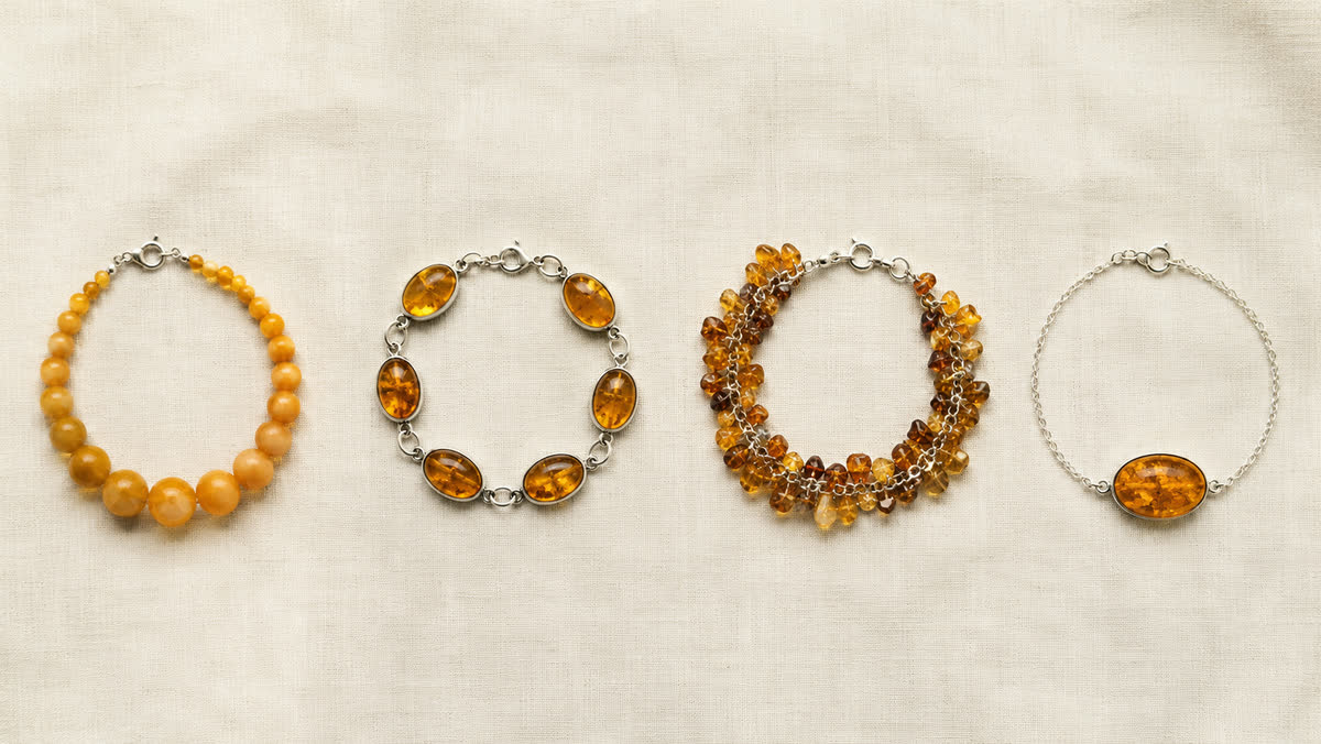 Vier Bernstein-Armband-Formate nebeneinander auf cremefarbenem Leinen: Perlen-Armband mit runden butterscotch-Beads, Cabochon-Reihe in Silberfassung, Cluster-Armband mit Bernstein-Splittern, Solitär an feiner Silberkette