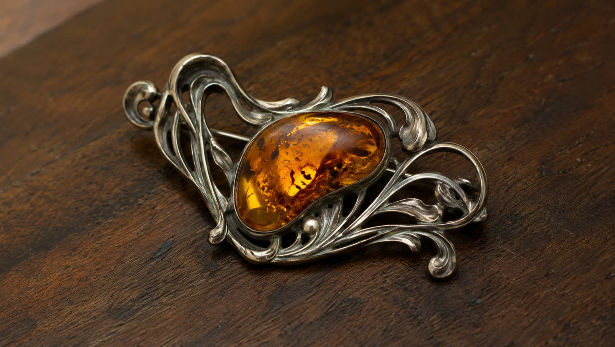 Antike Jugendstil-Brosche um 1910 mit organisch fließenden Silberranken, wie zarte Pflanzen-Tendrille, die einen unregelmäßig geformten honig-cognac Bernstein-Cabochon umrahmen, Silber zeigt schöne Alterspatina, auf warmem Walnussholz